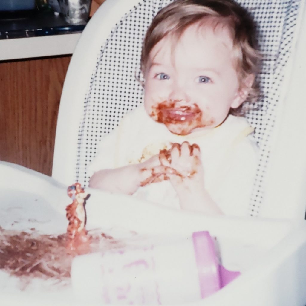 A baby sits in a high chair with a masterpiece created in Easy Yummy Edible Finger Paint for Little Artists.