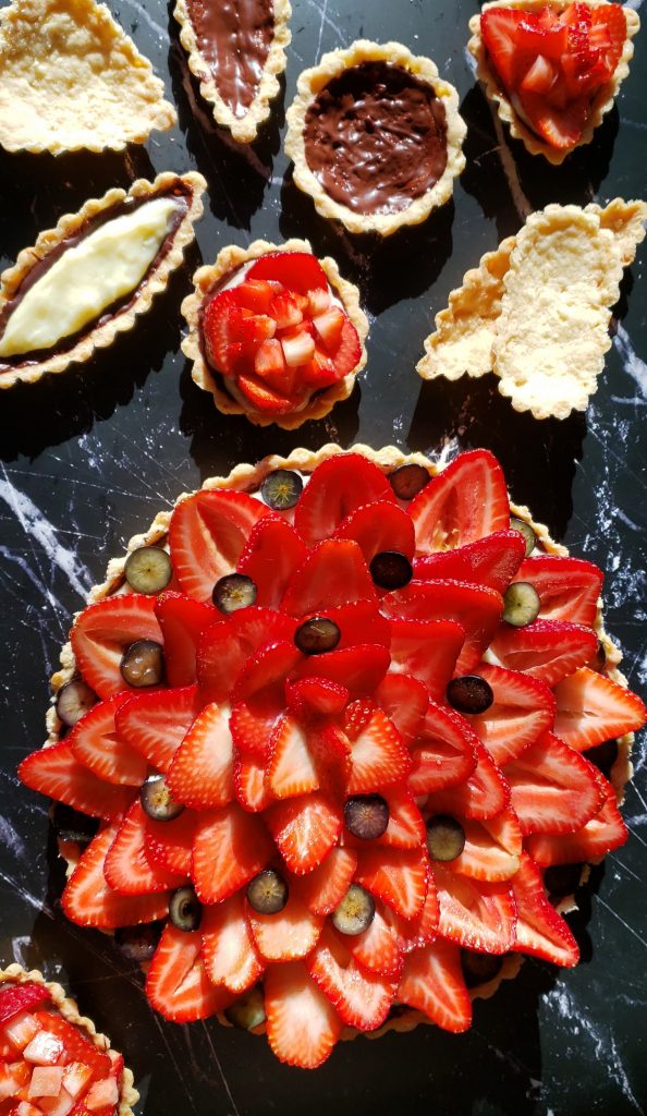 A closeup shot of this Beautiful 3 Step Seasonal Fresh Fruit Tart. A flaky shell is brushed with dark chocolate, then filled with a silky vanilla pastry cream and topped with fresh seasonal fruit. Strawberries adorn the top of the tart.